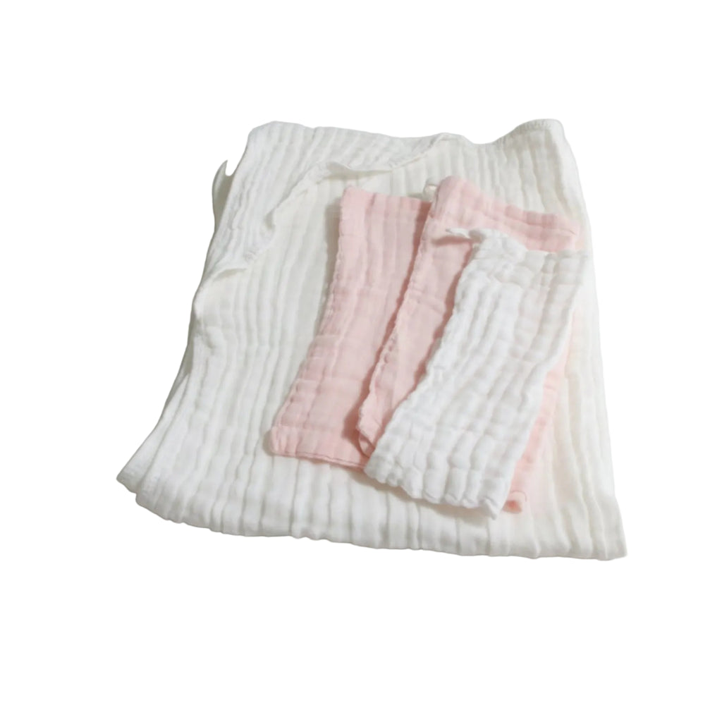 Folded baby clothes including a white ribbed top and pink pants on a light gray background
