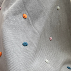 Gray knitted blanket with colorful dots on a gray surface