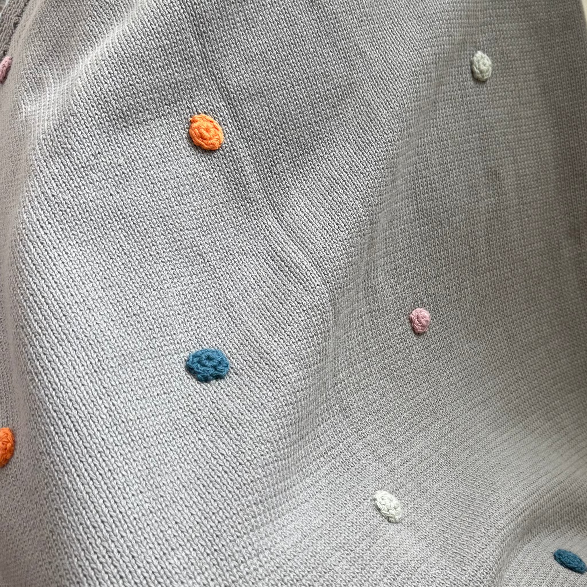 Gray knitted blanket with colorful dots on a gray surface