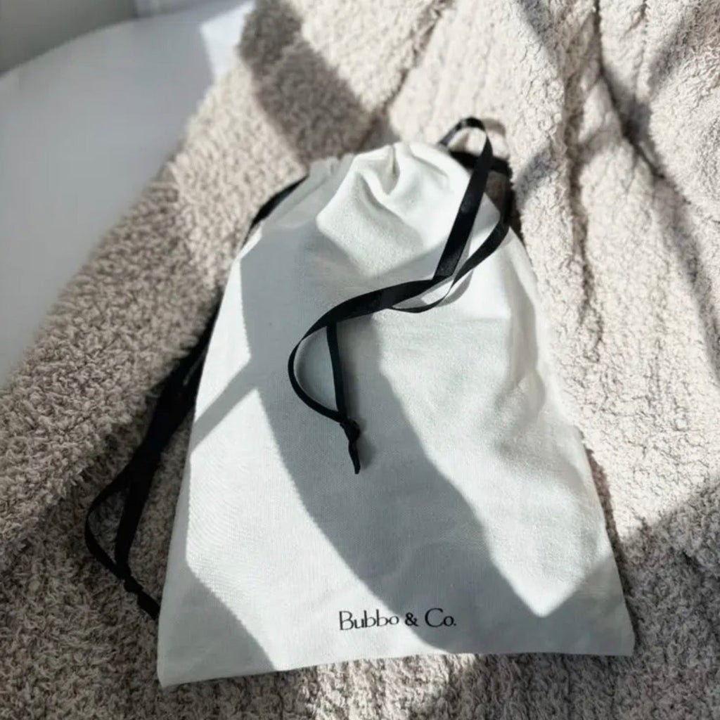 White drawstring bag with black drawstring on a textured surface, featuring the brand 'Bobbi & Co'.