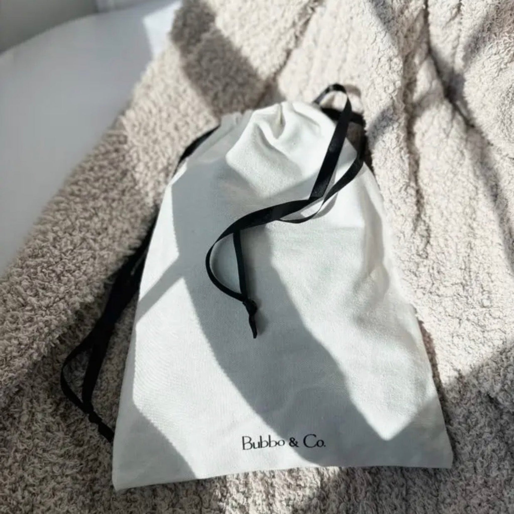 White drawstring bag with black drawstring on a textured surface, featuring the brand 'Bobbi & Co'.