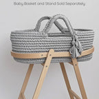 Gray woven baby basket on a wooden stand with text indicating separate purchase for basket and stand.