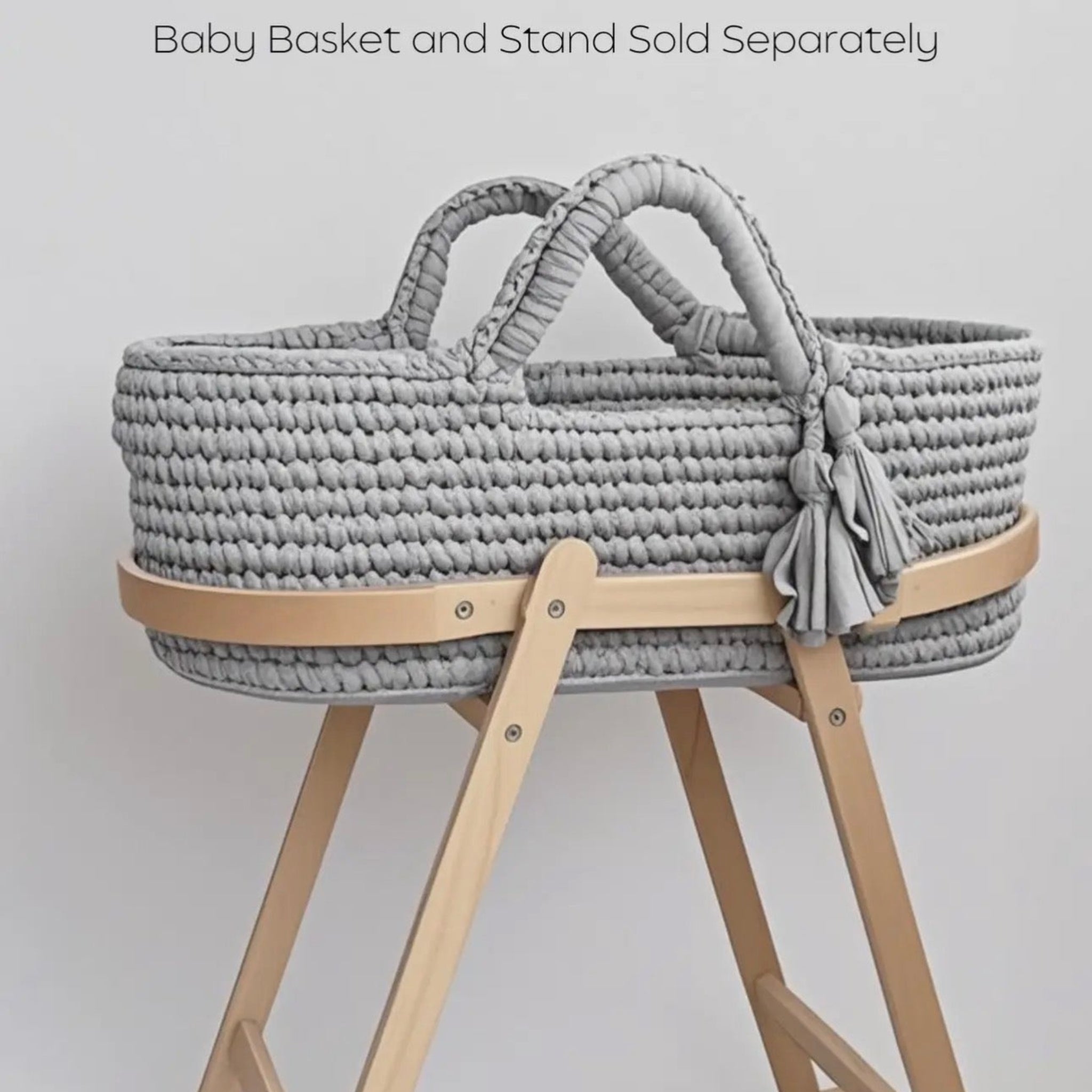 Gray woven baby basket on a wooden stand with text indicating separate purchase for basket and stand.