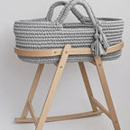 Gray woven baby basket on a wooden stand with text indicating separate purchase for basket and stand.