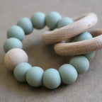 Teething ring with green beads and wooden handle on a beige background