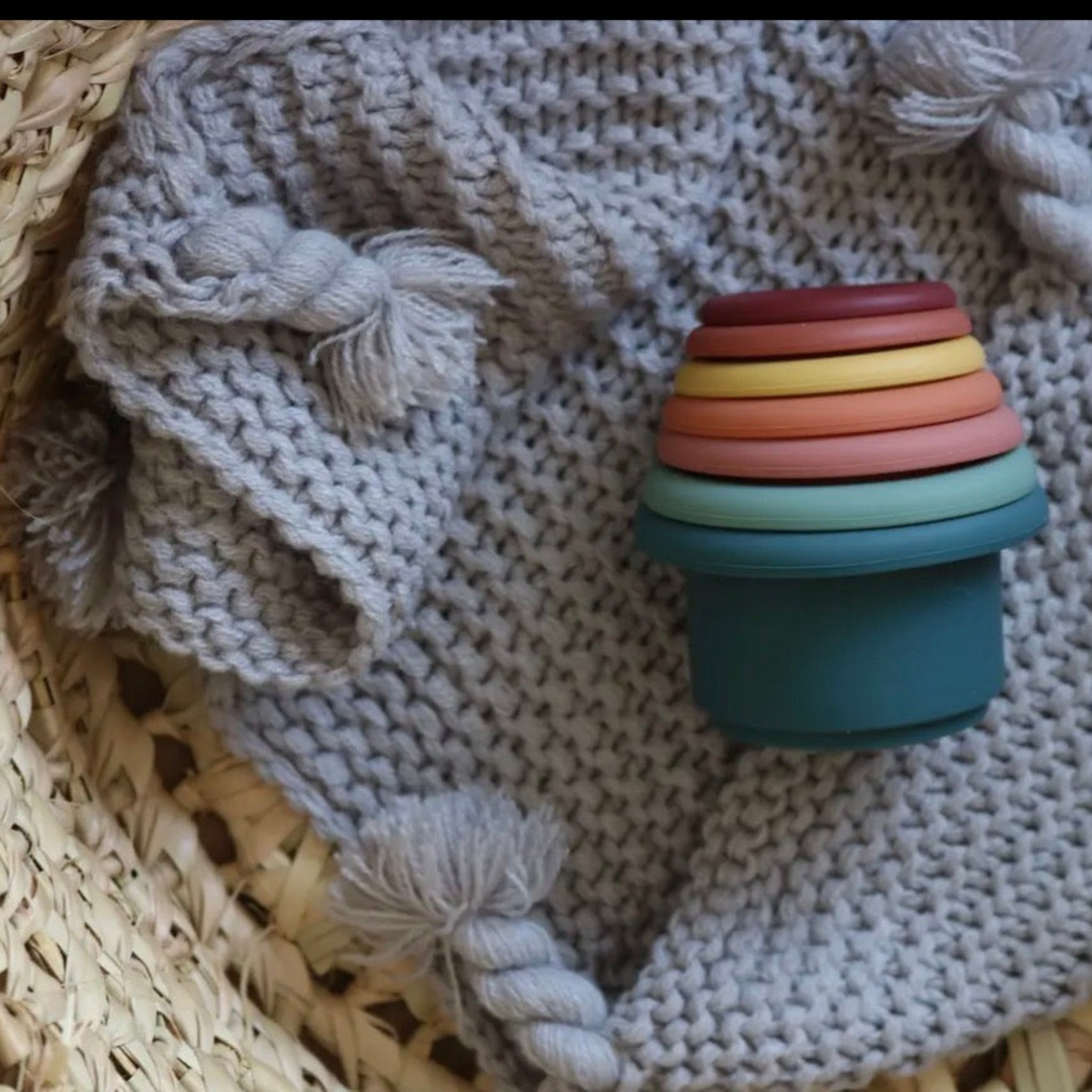 Colorful stackable toy on a textured surface with a woven basket