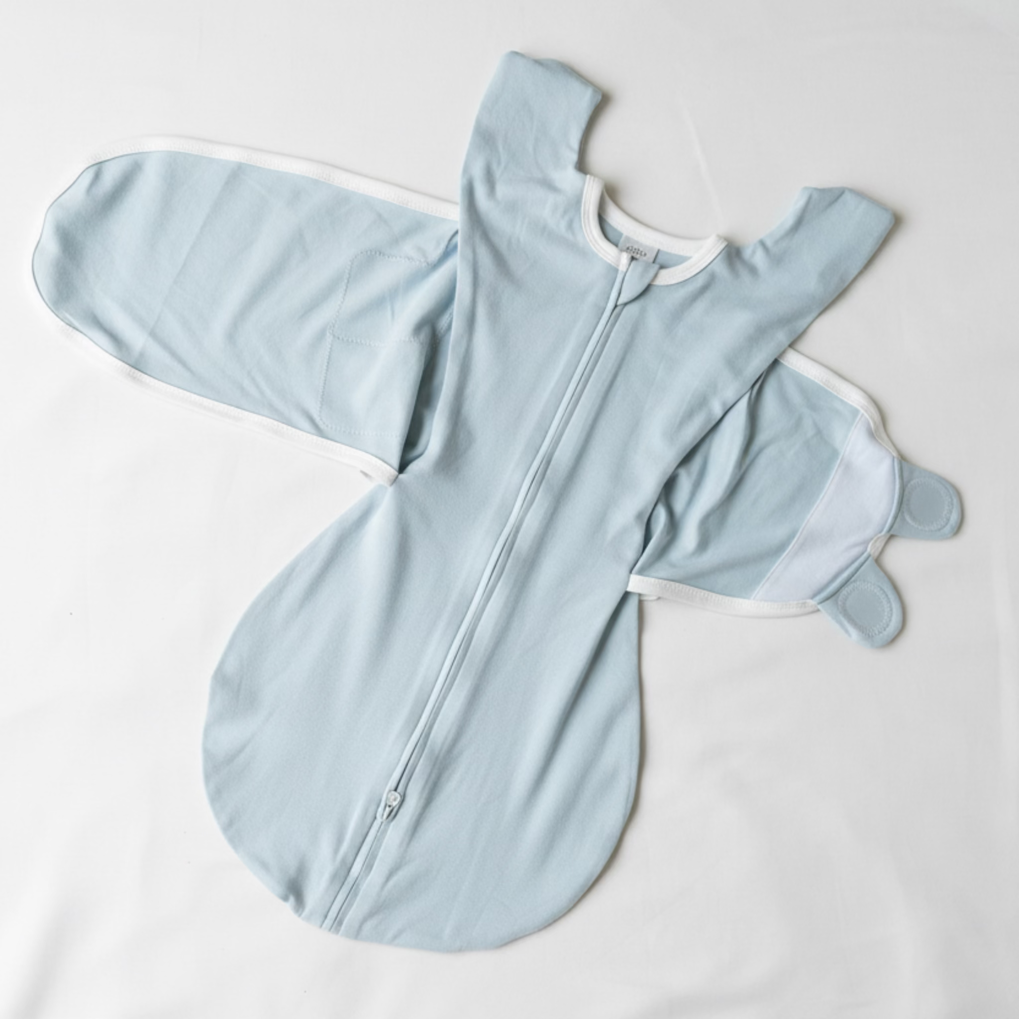 Light blue baby onesie with mittens on a beige surface