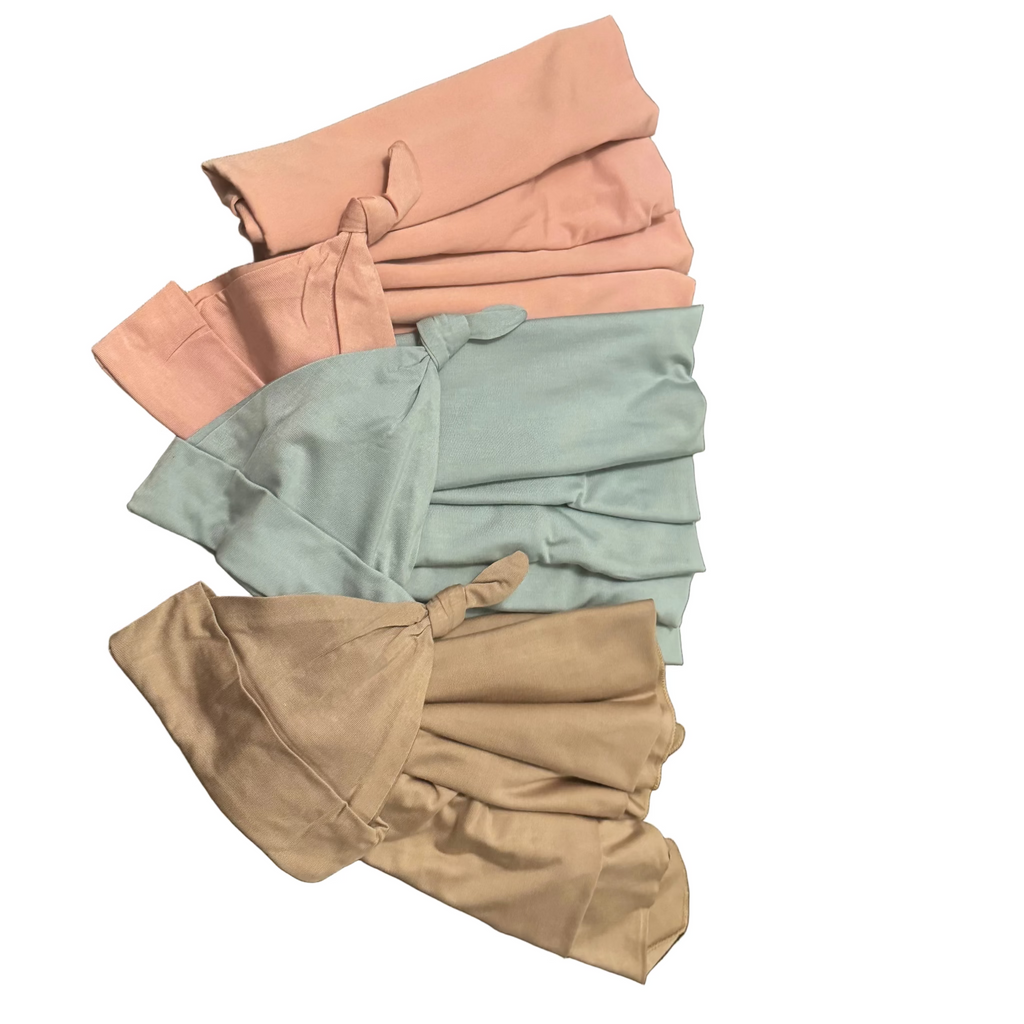Three folded pieces of swaddles in pink, blue green, and beige on a wooden surface